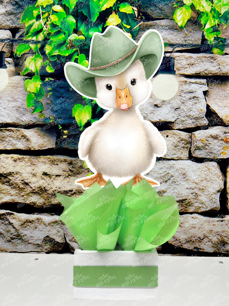 fully assembled party centerpieces featuring adorable watercolor-style white baby geese or ducklings dressed in pink outfits. The designs include Goose w/ Bonnet, Goose w/ Boots, Goose w/Cowboy Hat, Goose w/ Overalls, Goose Standing, Goose on Swing. Each cutout stands on a white base wrapped in green ribbon with fluffy green tissue paper
