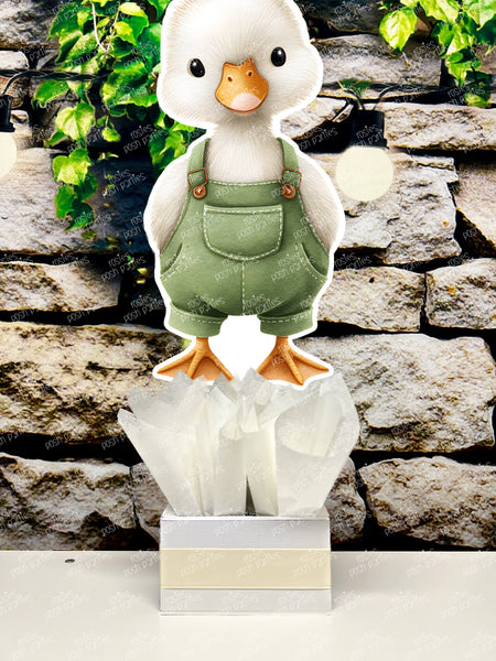 fully assembled party centerpieces featuring adorable watercolor-style white baby geese or ducklings dressed in pink outfits. The designs include Goose w/ Bonnet, Goose w/ Boots, Goose w/Cowboy Hat, Goose w/ Overalls, Goose Standing, Goose on Swing. Each cutout stands on a white base wrapped in green ribbon with fluffy green tissue paper