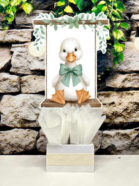 fully assembled party centerpieces featuring adorable watercolor-style white baby geese or ducklings dressed in pink outfits. The designs include Goose w/ Bonnet, Goose w/ Boots, Goose w/Cowboy Hat, Goose w/ Overalls, Goose Standing, Goose on Swing. Each cutout stands on a white base wrapped in green ribbon with fluffy green tissue paper