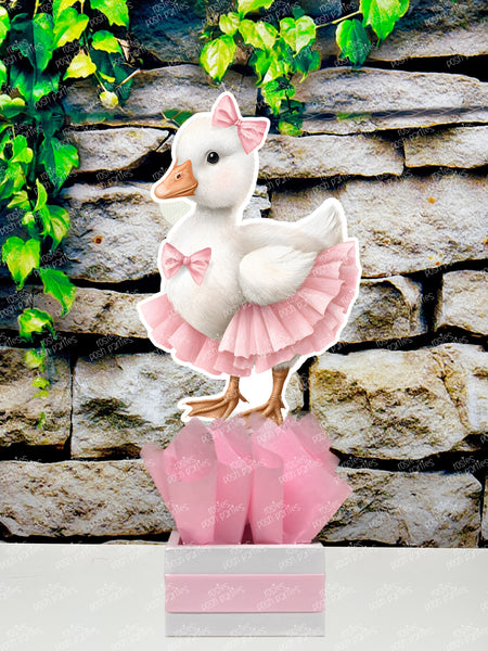 fully assembled party centerpieces featuring adorable watercolor-style white baby geese or ducklings dressed in pink outfits. The designs include a goose in pink boots, a pink sunhat, a pink cowboy hat, a pink tutu, a large pink bow, and one inside a pink floral frame. Each cutout stands on a white base wrapped in pink ribbon with fluffy pink tissue paper.